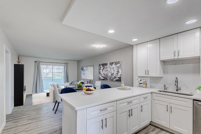 kitchen with dishwasher, kitchen peninsula, sink, light wood-type flooring, and white cabinetry