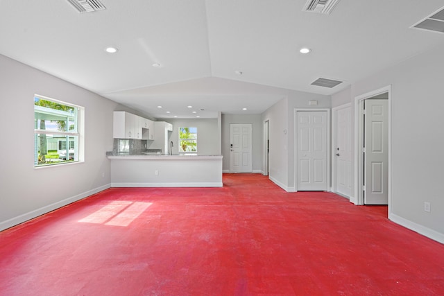 unfurnished living room with sink, light colored carpet, a healthy amount of sunlight, and vaulted ceiling