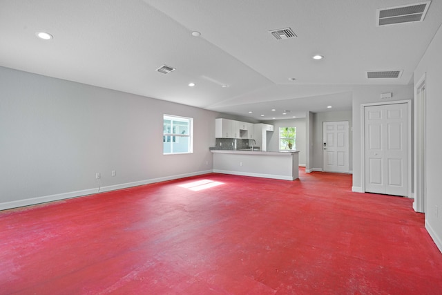 unfurnished living room featuring light colored carpet, lofted ceiling, and sink