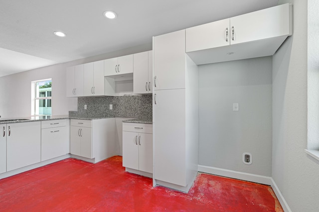 kitchen with dark stone countertops, white cabinetry, and backsplash