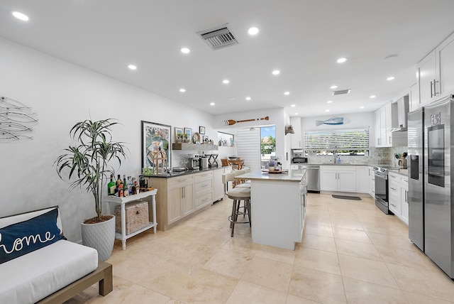 1484 Via Del Sol, Jupiter, FL 33477 - kitchen featuring stainless steel appliances, a breakfast bar area, backsplash, white cabinetry, and wall chimney range hood
