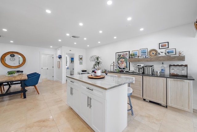 kitchen featuring a kitchen island, light stone counters, light tile patterned flooring, a kitchen bar, and white cabinets