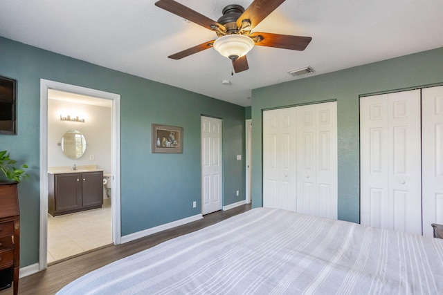 bedroom featuring sink, dark wood-type flooring, two closets, ceiling fan, and ensuite bathroom