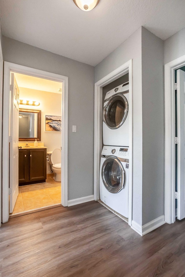 clothes washing area with stacked washer / dryer, sink, and light hardwood / wood-style flooring