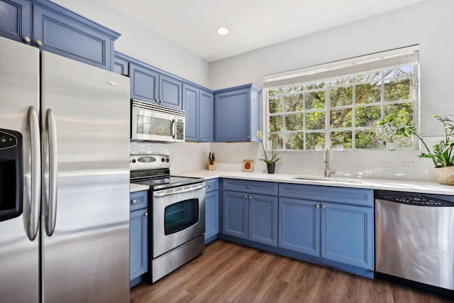 kitchen with sink, appliances with stainless steel finishes, tasteful backsplash, blue cabinetry, and dark wood-type flooring