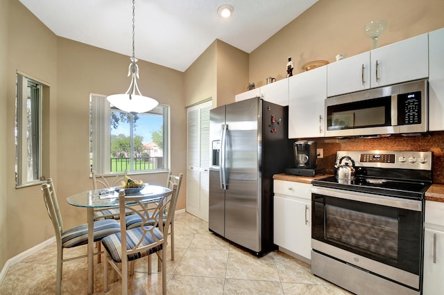 kitchen with appliances with stainless steel finishes, light tile patterned floors, lofted ceiling, white cabinets, and pendant lighting