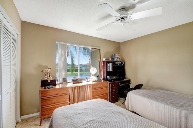 bedroom with a textured ceiling, light colored carpet, ceiling fan, and a closet