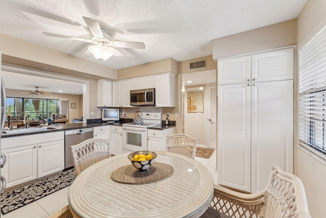 kitchen with white cabinets, light tile patterned floors, a textured ceiling, kitchen peninsula, and stainless steel appliances