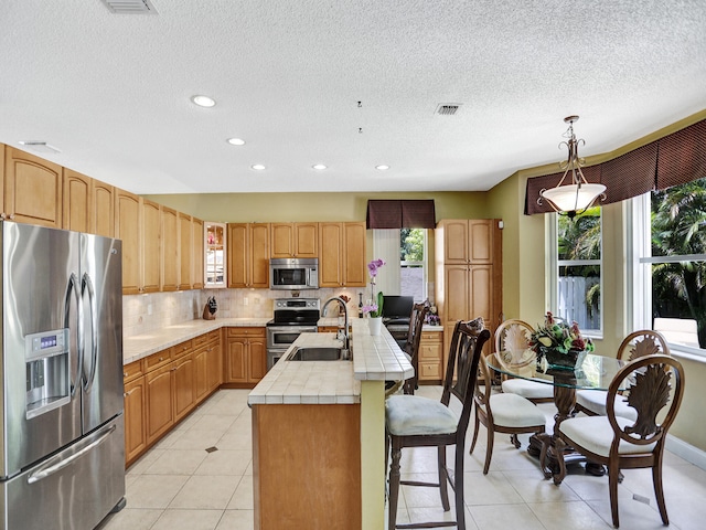 kitchen featuring stainless steel appliances, sink, a kitchen island with sink, tile counters, and pendant lighting