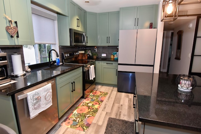 kitchen with green cabinetry, stainless steel appliances, dark stone counters, sink, and light hardwood / wood-style flooring