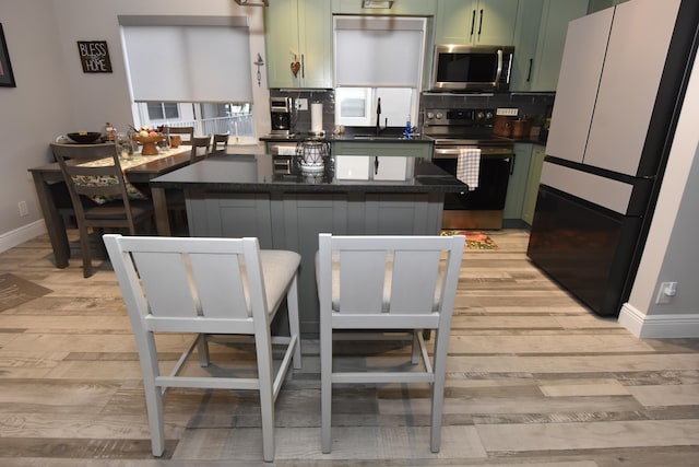 kitchen featuring tasteful backsplash, appliances with stainless steel finishes, a kitchen bar, green cabinetry, and light hardwood / wood-style flooring