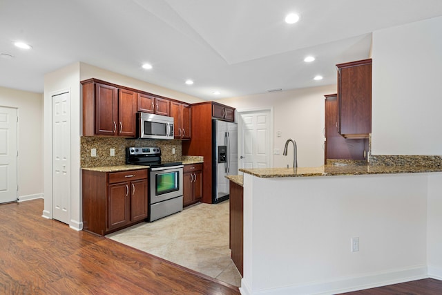 kitchen featuring kitchen peninsula, appliances with stainless steel finishes, light stone counters, and light wood-type flooring