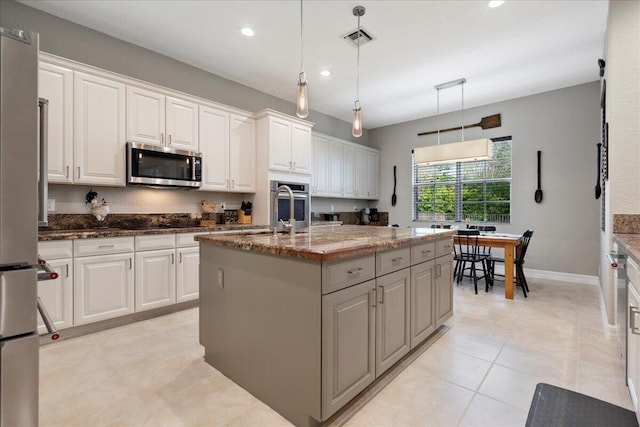 kitchen with pendant lighting, appliances with stainless steel finishes, white cabinetry, and an island with sink