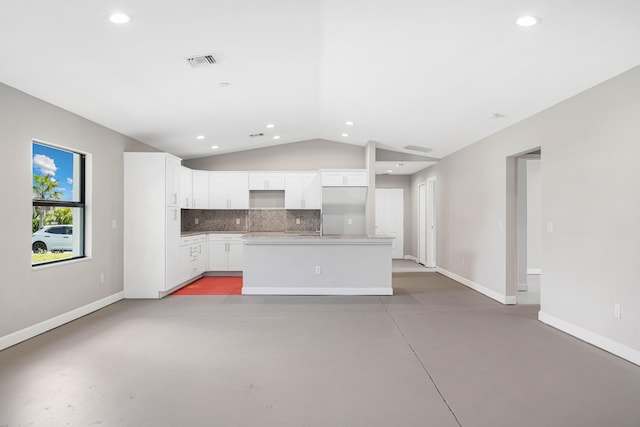 kitchen featuring lofted ceiling, a center island with sink, white cabinets, decorative backsplash, and concrete flooring