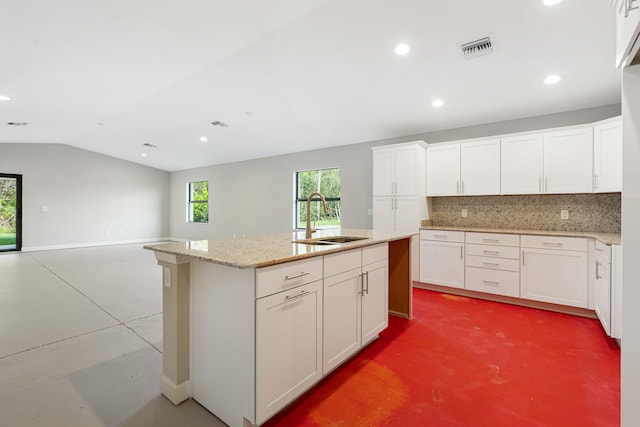 kitchen featuring concrete floors, sink, tasteful backsplash, an island with sink, and white cabinetry