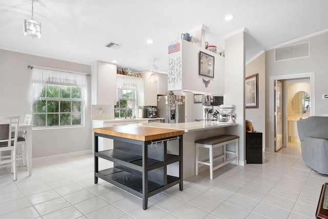 kitchen with kitchen peninsula, ornamental molding, light tile patterned floors, white cabinets, and stainless steel fridge with ice dispenser