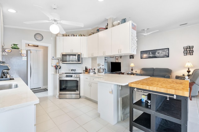 kitchen featuring kitchen peninsula, appliances with stainless steel finishes, light tile patterned floors, crown molding, and white cabinets