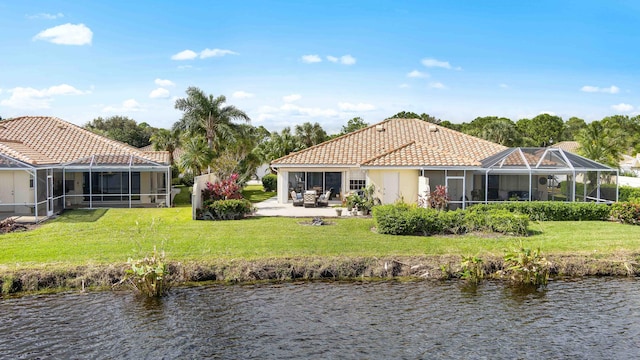 rear view of house with glass enclosure, a water view, and a lawn