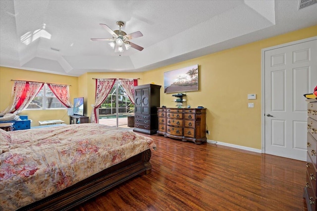 bedroom featuring a textured ceiling, ceiling fan, dark wood-type flooring, and a tray ceiling