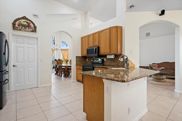 kitchen featuring sink, dark stone counters, decorative backsplash, light tile patterned floors, and black appliances