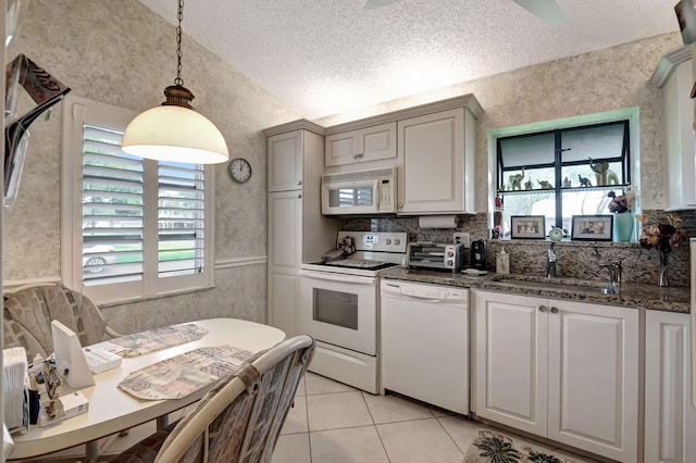 kitchen featuring dark stone counters, a textured ceiling, light tile patterned floors, pendant lighting, and white appliances