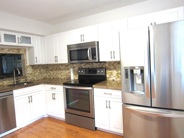 kitchen with sink, dark stone countertops, white cabinets, stainless steel appliances, and light wood-type flooring