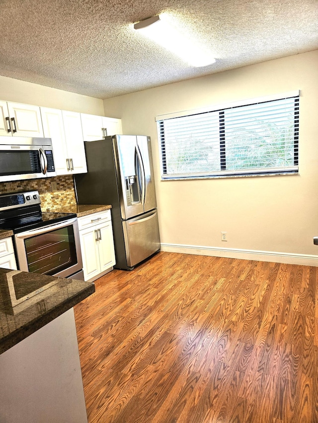 kitchen featuring appliances with stainless steel finishes, light wood-type flooring, backsplash, white cabinets, and a textured ceiling