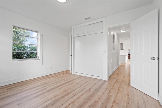 unfurnished bedroom featuring a textured ceiling, light wood-type flooring, and a closet