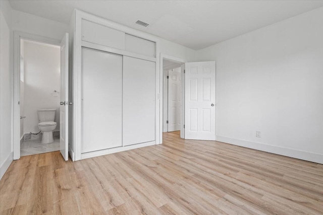 unfurnished bedroom with ensuite bath, a closet, and light hardwood / wood-style flooring