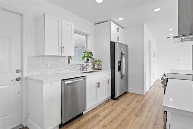 kitchen featuring light wood-type flooring, stainless steel appliances, sink, exhaust hood, and white cabinetry