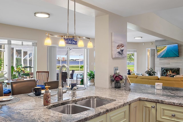 kitchen with sink, light stone countertops, hanging light fixtures, and cream cabinets