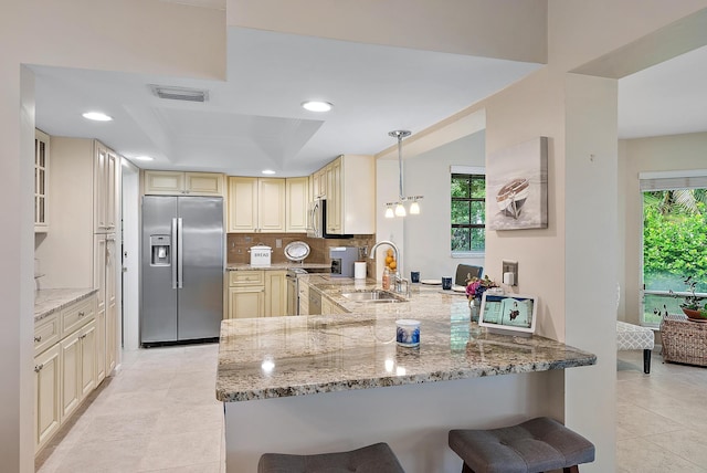 kitchen with kitchen peninsula, light stone counters, pendant lighting, and appliances with stainless steel finishes