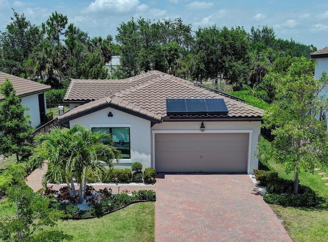 mediterranean / spanish home with stucco siding, a tile roof, decorative driveway, a garage, and solar panels