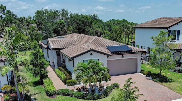 mediterranean / spanish-style house featuring stucco siding, a tile roof, decorative driveway, roof mounted solar panels, and a garage