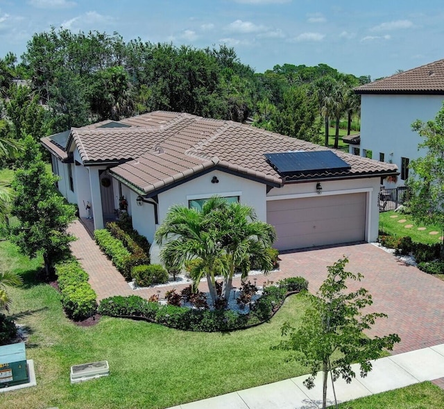 mediterranean / spanish house featuring a front yard, solar panels, an attached garage, and a tiled roof