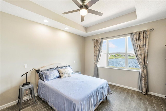 bedroom with a water view, a raised ceiling, ceiling fan, and dark hardwood / wood-style floors