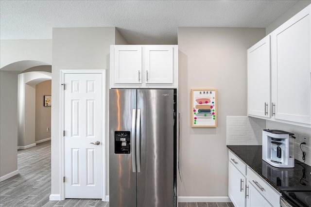 kitchen featuring white cabinetry, stainless steel refrigerator with ice dispenser, a textured ceiling, light wood-type flooring, and decorative backsplash