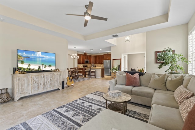 living room with ceiling fan with notable chandelier, plenty of natural light, and a tray ceiling