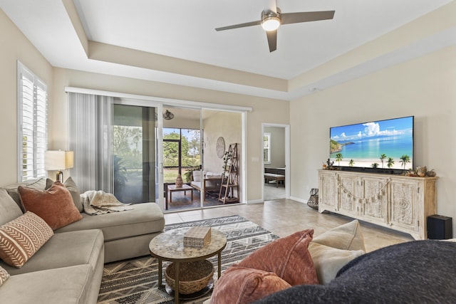 living room with baseboards, a raised ceiling, a ceiling fan, and tile patterned floors