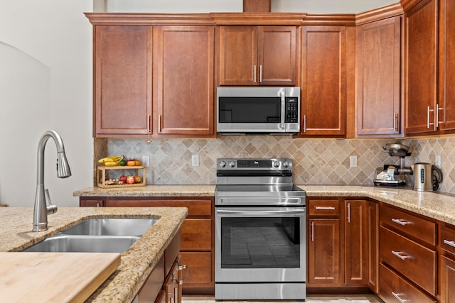 kitchen with light stone counters, sink, backsplash, and stainless steel appliances