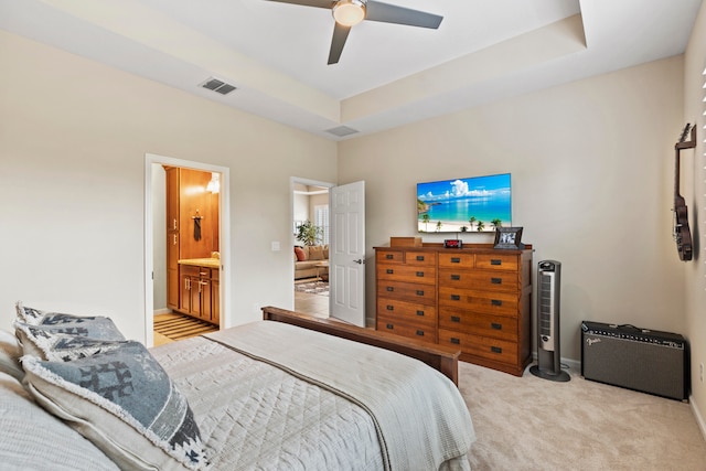 bedroom featuring ceiling fan, ensuite bathroom, light colored carpet, and a tray ceiling