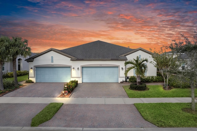 ranch-style house featuring a garage, decorative driveway, a lawn, and stucco siding