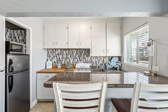 kitchen with white cabinets, sink, appliances with stainless steel finishes, tasteful backsplash, and a kitchen bar