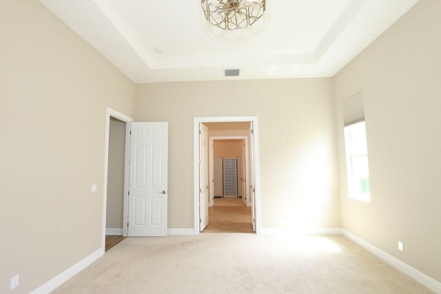 unfurnished bedroom featuring light colored carpet and a raised ceiling