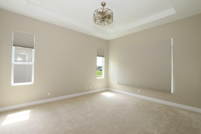 carpeted spare room with a chandelier and a tray ceiling