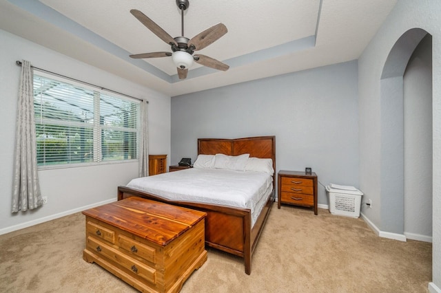 carpeted bedroom with ceiling fan and a tray ceiling