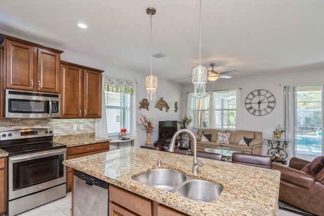 kitchen featuring appliances with stainless steel finishes, light stone countertops, hanging light fixtures, decorative backsplash, and sink