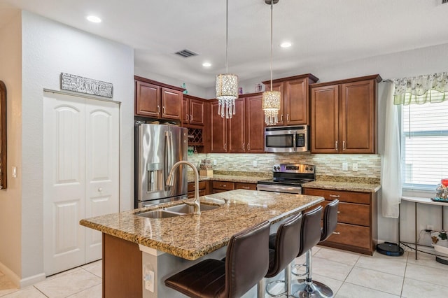 kitchen with appliances with stainless steel finishes, a kitchen bar, hanging light fixtures, sink, and a kitchen island with sink