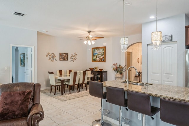 kitchen with sink, light stone counters, ceiling fan, light tile patterned floors, and hanging light fixtures