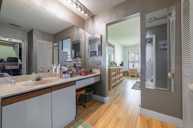 full bathroom featuring a closet, a textured ceiling, vanity, wood finished floors, and baseboards